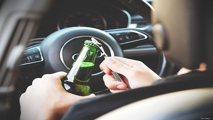 Rückansicht einer Person hinter dem Steuer mit einer Flasche Bier in der Hand