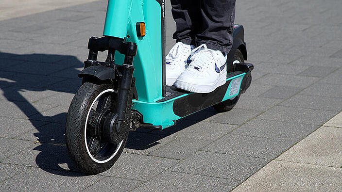 Nahaufnahme der beiden Turnschuhe einer Person, die auf einem E-Scooter steht.