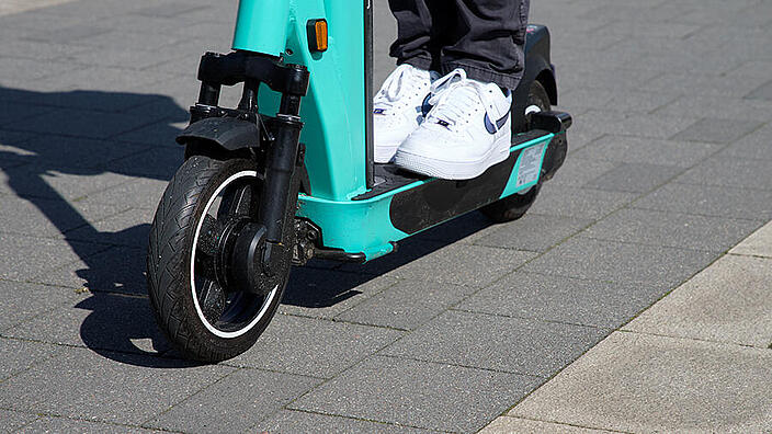 Nahaufnahme der beiden Turnschuhe einer Person, die auf einem E-Scooter steht.