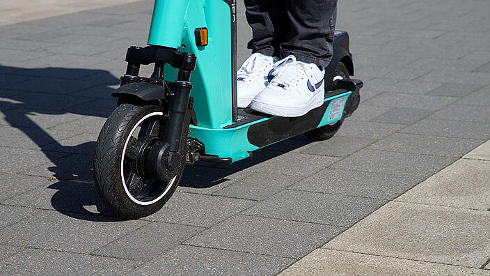 Nahaufnahme der beiden Turnschuhe einer Person, die auf einem E-Scooter steht.