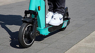 Nahaufnahme der beiden Turnschuhe einer Person, die auf einem E-Scooter steht.