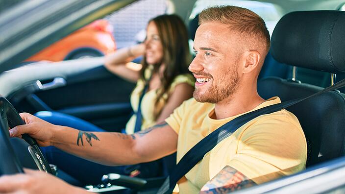 Junger Mann fährt Auto, neben ihm eine junge Frau.