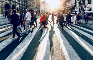 Viele Menschen laufen in einer Stadt bei Sonnenuntergang über einen Zebrastreifen.