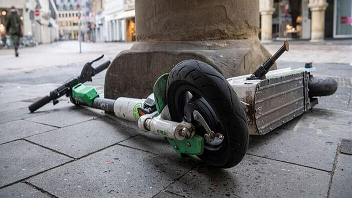 Auf dem Fußweg liegender E-Scooter neben einer Säule.