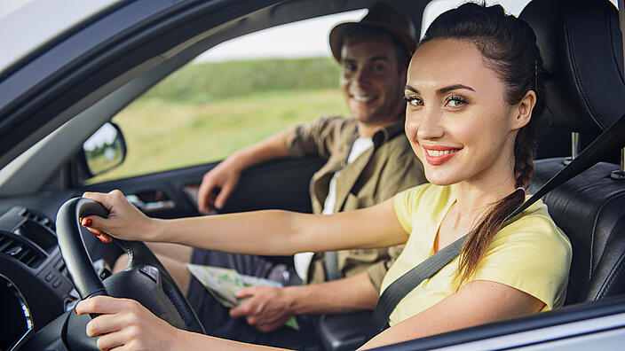 Junge Frau fährt Auto, neben ihr ein junger Mann