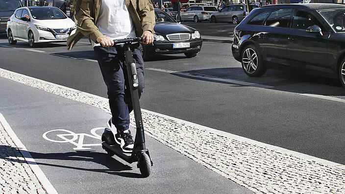 Ein Mann fährt mit einem E-Scooter auf einem Radweg. Er trägt einen Helm.