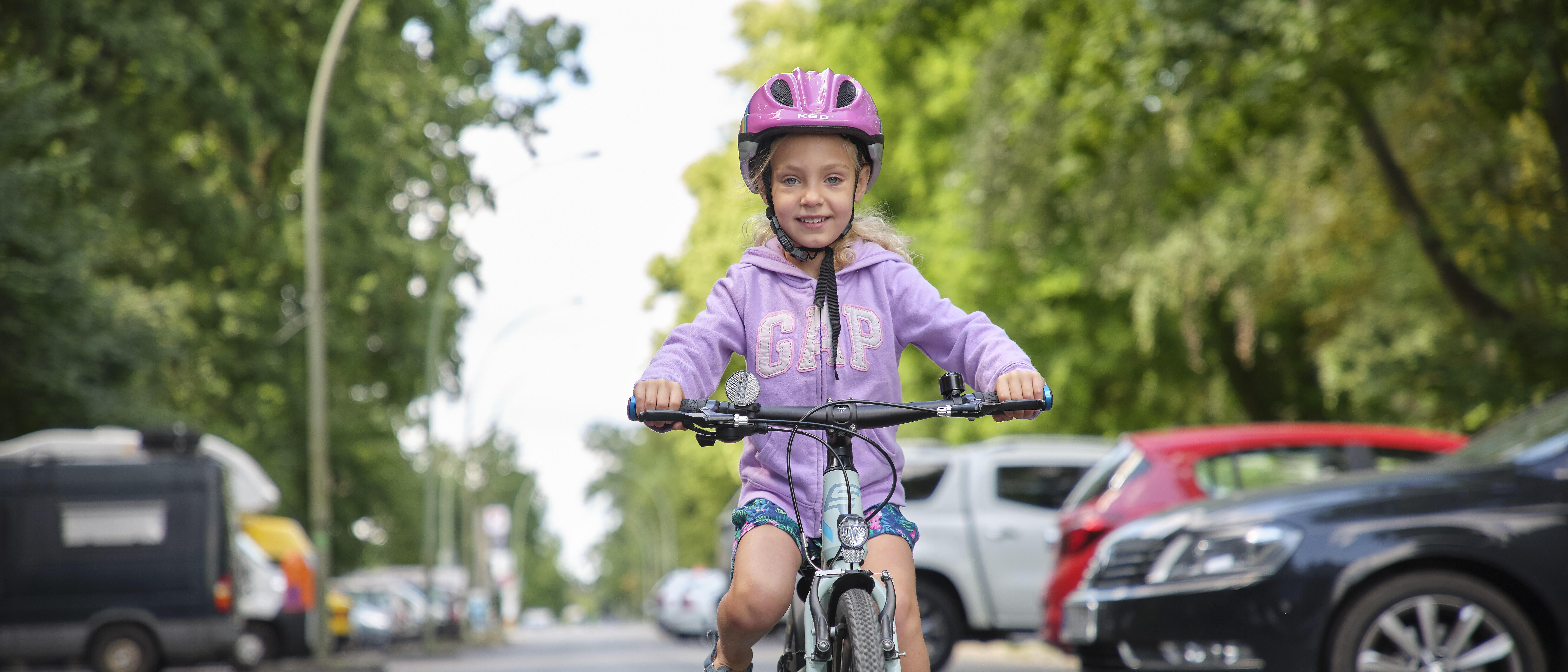 Ein Mädchen fährt auf einem Fahrrad. Sie trägt einen rosa Helm.