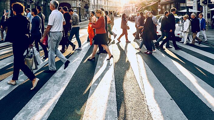 Viele Menschen laufen in einer Stadt bei Sonnenuntergang über einen Zebrastreifen.