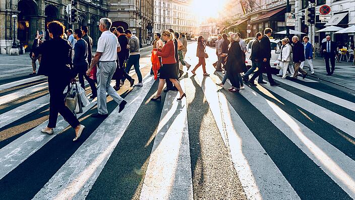 Viele Menschen laufen in einer Stadt bei Sonnenuntergang über einen Zebrastreifen.