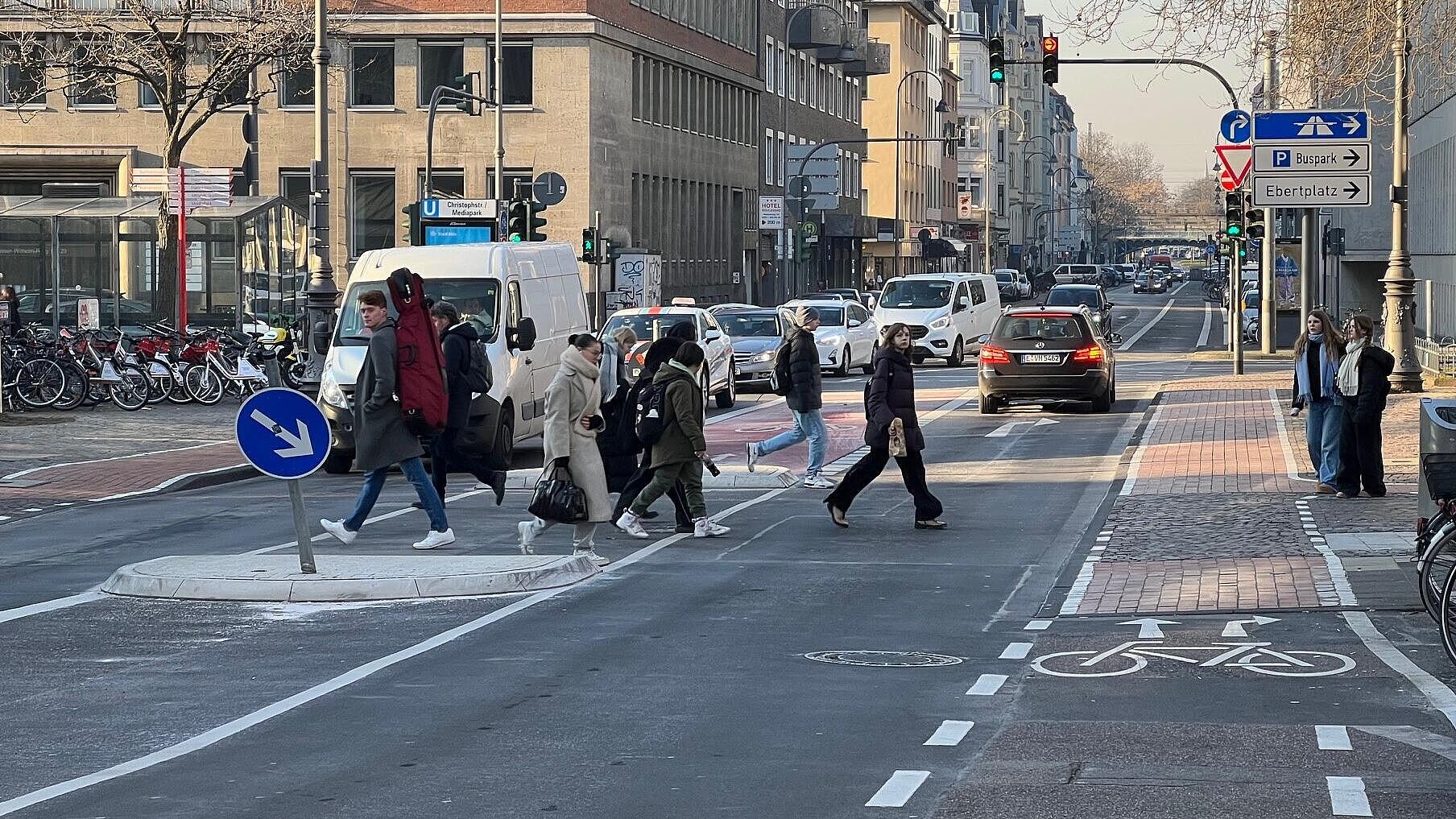 Querende Radverkehrsachse im Zuge einer radialen Hauptverkehrsstraße: Aufhebung der Linksabbiegestreifen für den Kfz-Verkehr zugunsten einer rot eingefärbten Aufstellfläche in Fahrbahnmitte mit separatem Fahrradsignal für den Radverkehr geradeaus in die Gladbacher Straße