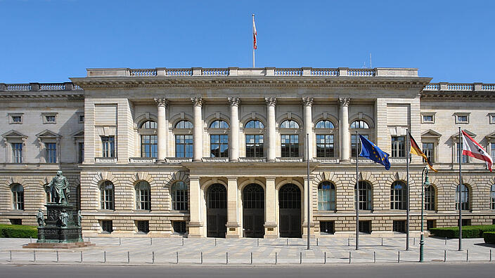 Abgeordnetenhaus von Berlin von vorne, blauer Himmel, rechts wehen die EU-, Deutschand- und Berlin-Flaggen