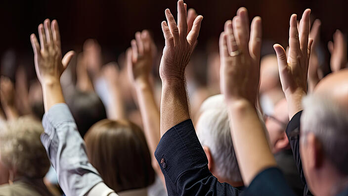 A diverse audience raises their hands in an important decision.