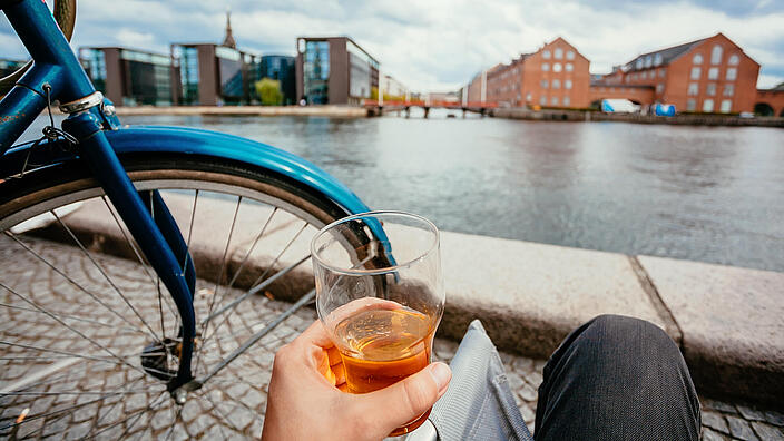 Beer glass of drinker and cityscape, water channel, old buildings of Copenhagen, Denmark