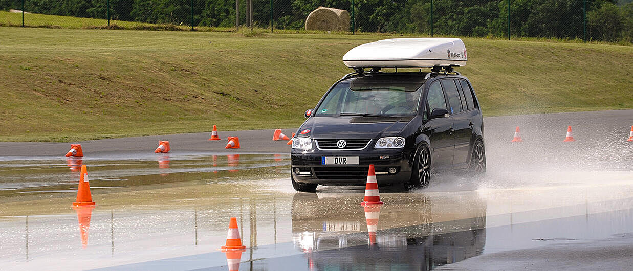 Auto fährt in einem Training über eine nasse Straße mit Dachbox