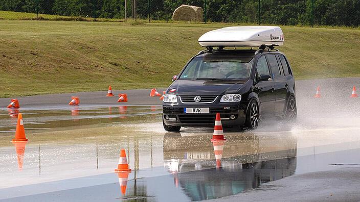 Auto fährt in einem Training über eine nasse Straße mit Dachbox