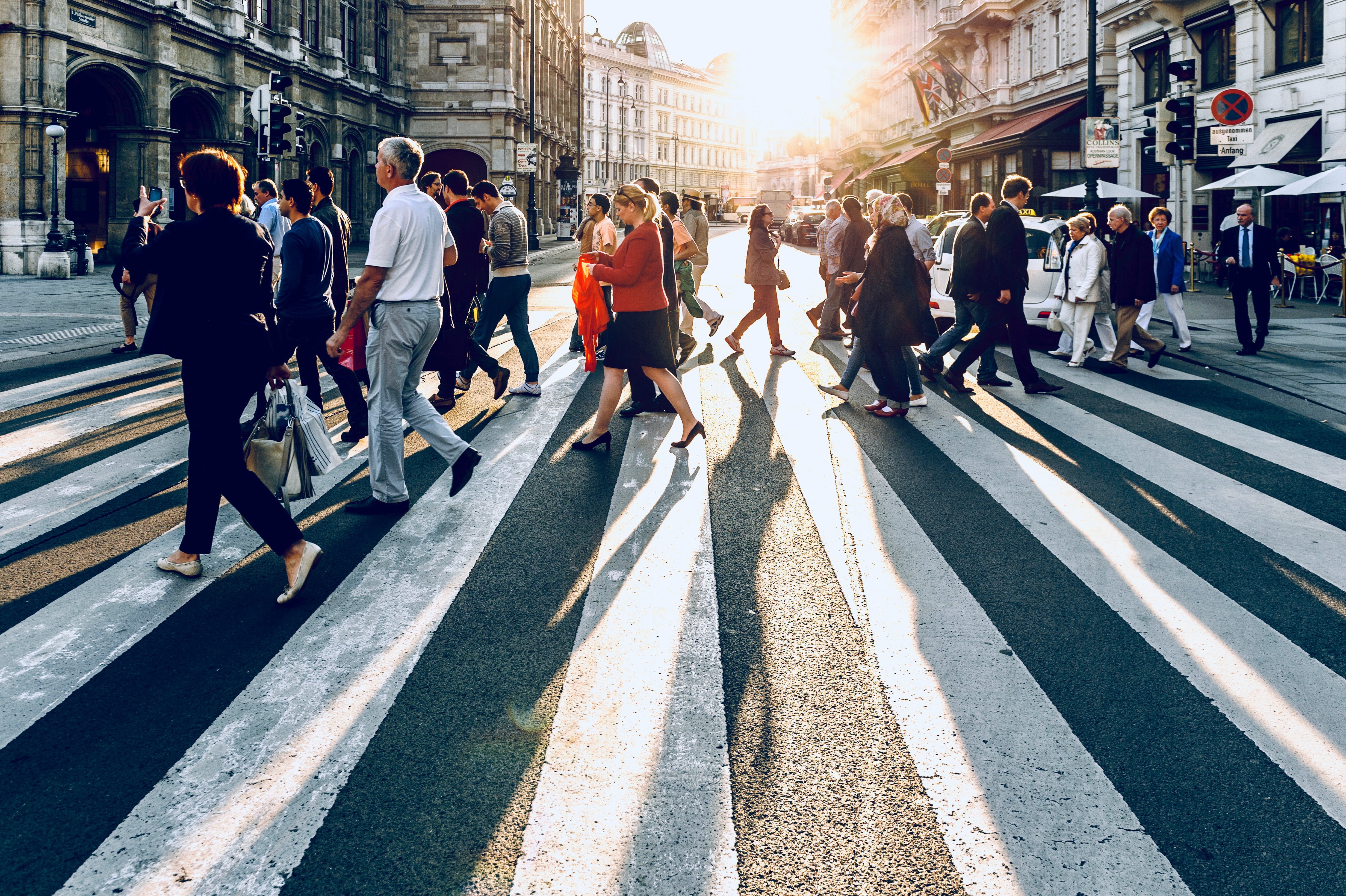 Viele Menschen laufen in einer Stadt bei Sonnenuntergang über einen Zebrastreifen.